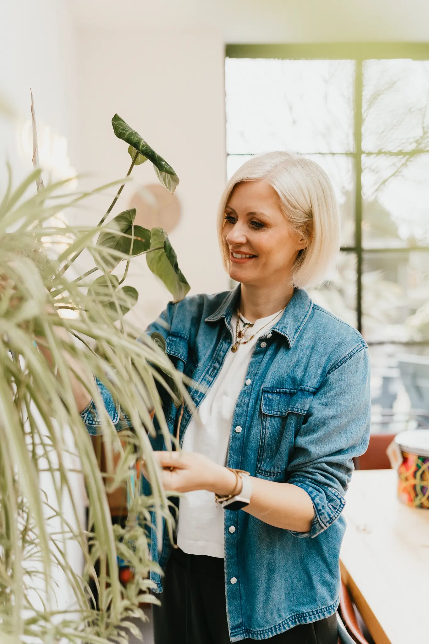 Lucy Nash tending a houseplant in a denim shirt