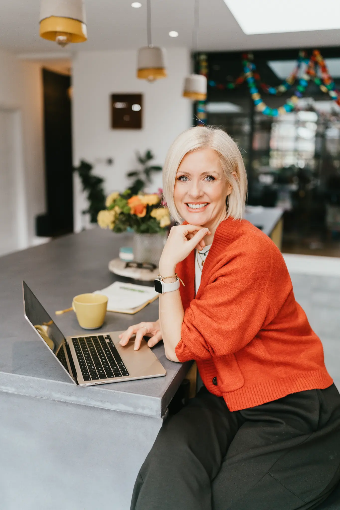 Lucy Nash working at a laptop with coffee, wearing an orange cardigan